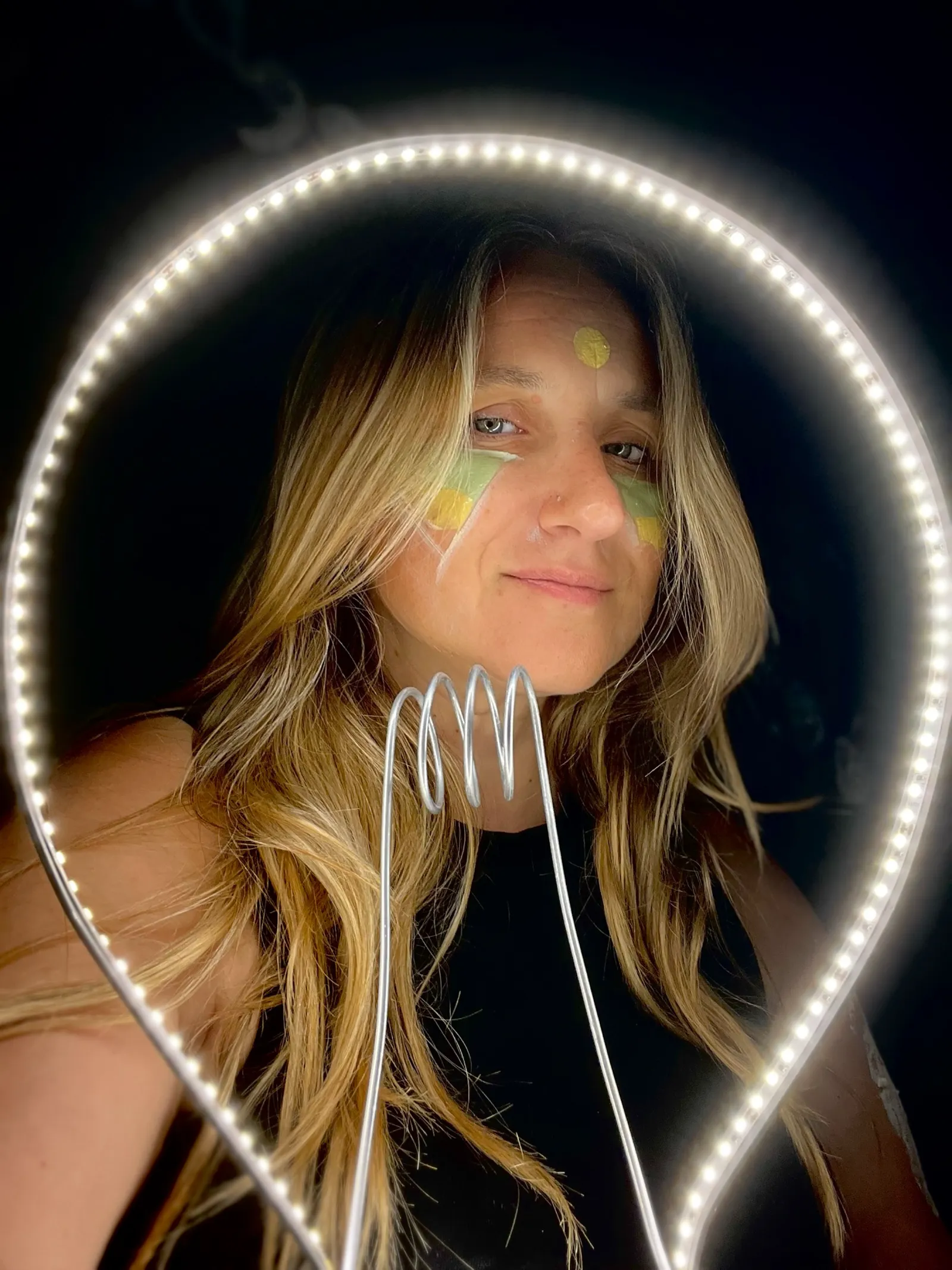 Anna Morchio dietro un anello luminoso, con cuori gialli dipinti sul viso, sorridente